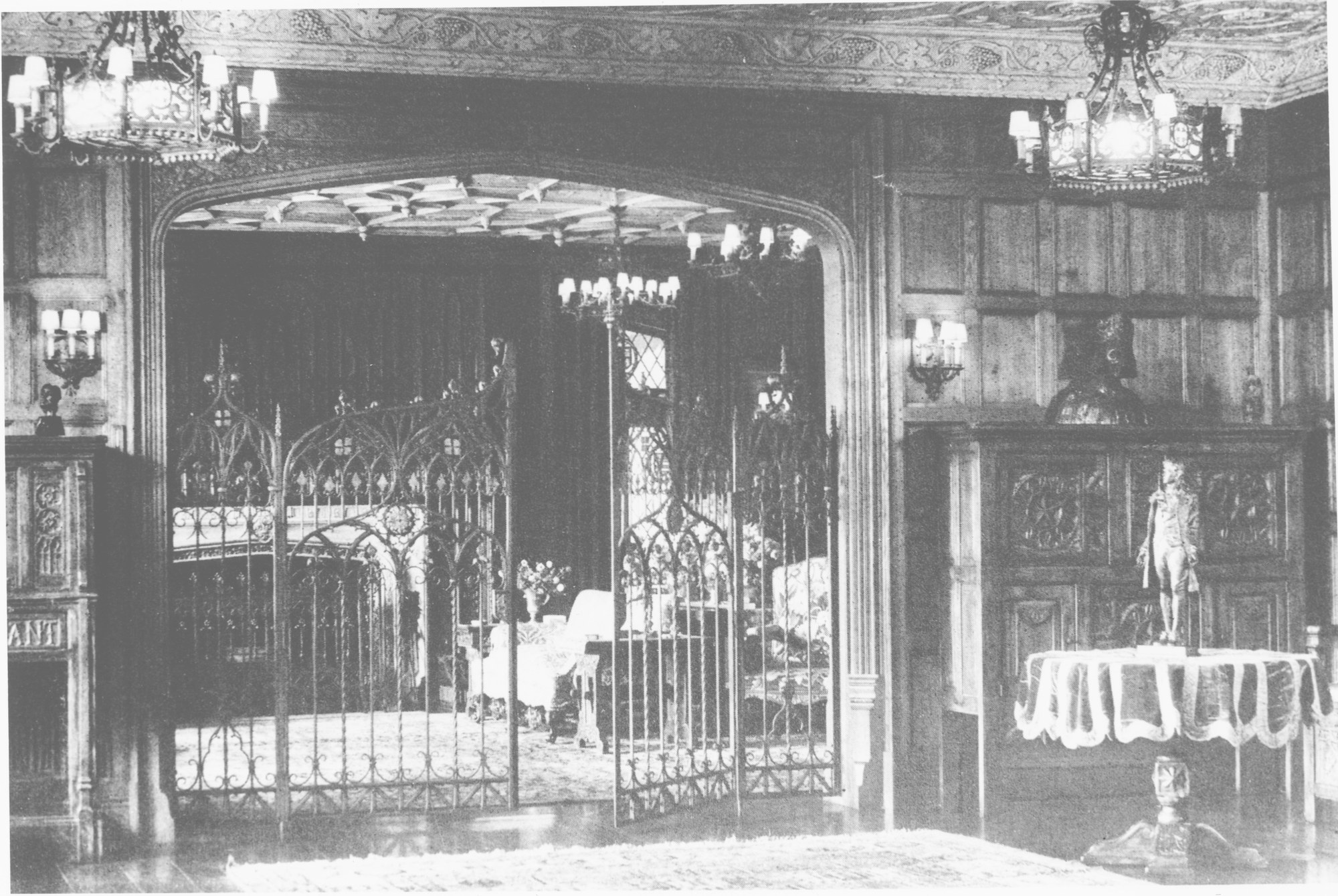 The Manor House interior featuring Gothic wrought-iron gates, carved oak paneling, and ornate chandeliers — original 1925 craftsmanship